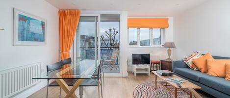 A modern living room with a glass dining table, a sofa, and a view of the city.