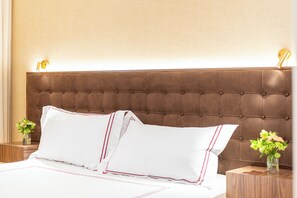 Una cama con ropa blanca y detalles rojos, un cabecero acolchado y dos mesitas de noche con jarrones de flores.