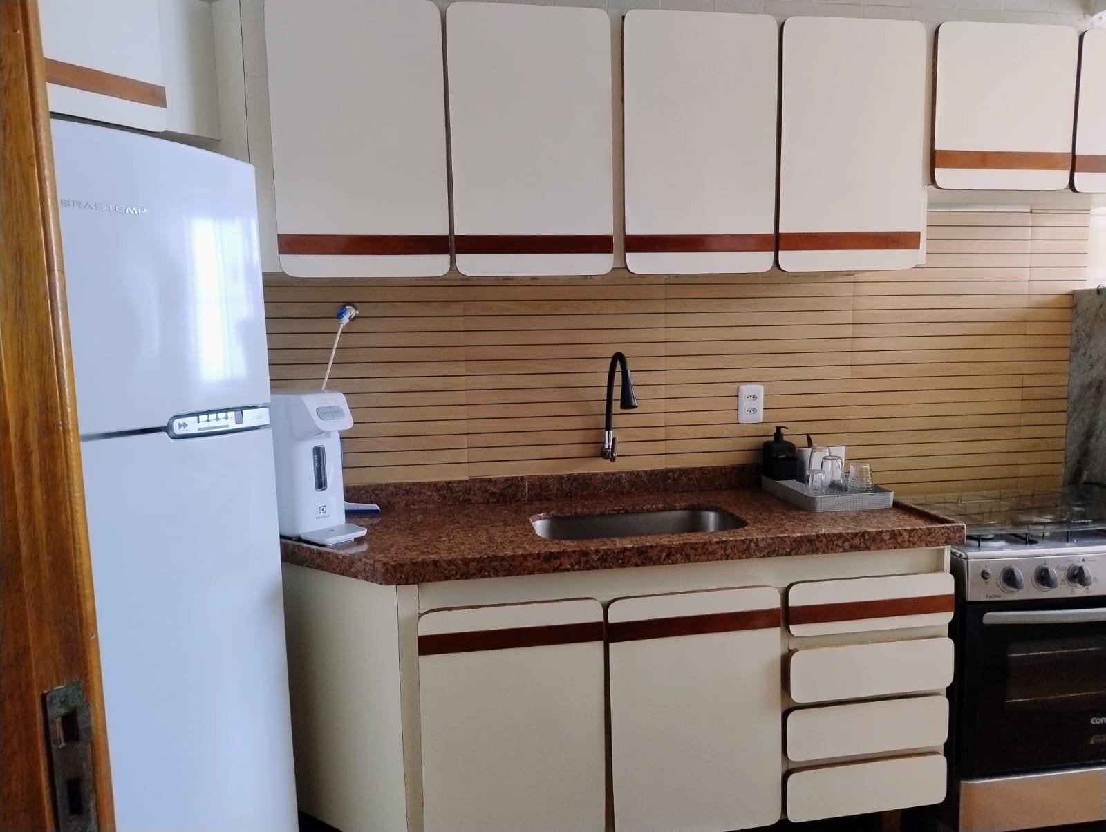 A kitchen with a white refrigerator, a coffee maker, a sink, and a stove.