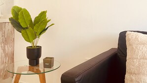 Ein modernes Wohnzimmer mit Glastisch, schwarzem Sofa, flauschigem weißen Überwurf und einer Topfpflanze.