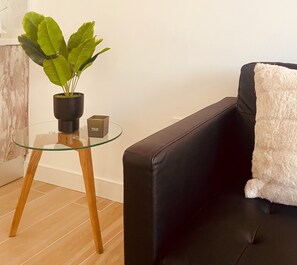 Ein modernes Wohnzimmer mit Glastisch, schwarzem Sofa, flauschigem weißen Überwurf und einer Topfpflanze.