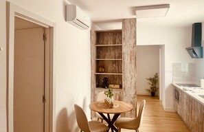 A modern kitchen with a built-in stove, a dining area with a round table and chairs, and a wooden shelving unit with decorative items. - Click&Guest - Doctoral Urbana 1 (Santa Lucía de Tirajana)