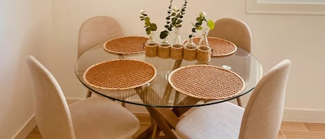 A round glass table with woven placemats and vases with plants, surrounded by chairs.