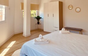 Ein Hotelzimmer mit einem Bett, einer Sitzbank, einem kleinen Tisch mit Pflanze und einem Spiegel an der Wand.