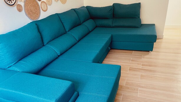 A teal sectional sofa in a room with wooden flooring and a wall decorated with woven wall art. - Click&Guest - Doctoral Urbana 2 (Santa Lucía de Tirajana)