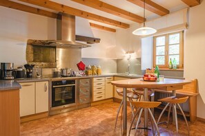 A kitchen with wooden beams, a stove, oven, and a dining area with chairs.