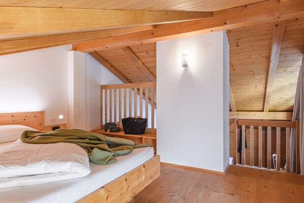 A bedroom with a wooden ceiling, a bed with white bedding, a nightstand, and a wall-mounted light.