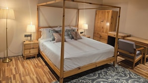 Una cama con dosel de madera, lámparas de noche, un escritorio con silla y una alfombra estampada.