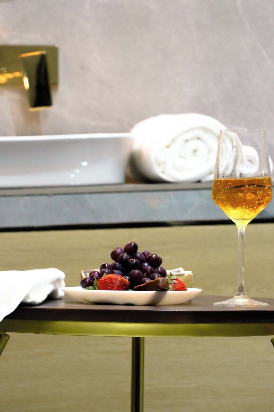 Una mesa con una copa de vino, un plato de uvas y una toalla enrollada en una habitación de hotel.