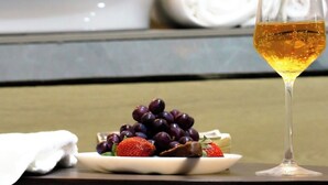 Una mesa con una copa de vino, un plato de uvas y una toalla enrollada en una habitación de hotel.