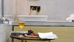 Un baño moderno con un lavabo blanco, un espejo y una pequeña mesa con una copa de vino, uvas y un libro.
