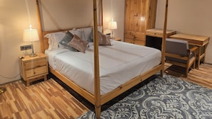 Una cama con dosel sobre un armazón de madera, una mesita de noche con lámpara, un guardarropa de madera y un escritorio con silla.