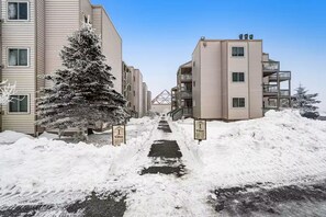 Een besneeuwde pad dat naar een woongebouw leidt, met balkons en een bord waarop 'Villas' staat.