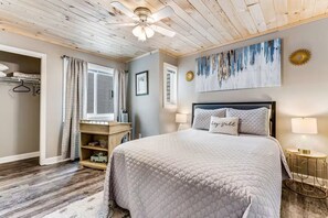 A bedroom with a bed, a ceiling fan, a window with curtains, a wall-mounted artwork, and a bedside lamp. - Ski, Soak & Relax | Cozy Beech Mountain Condo (Beech Mountain)