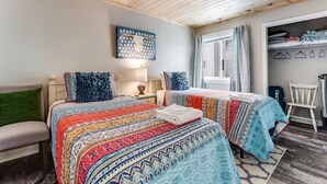 A bedroom with two beds, a wooden ceiling, a wall-mounted artwork, a window with curtains, and a closet with folded clothes. - Ski, Soak & Relax | Cozy Beech Mountain Condo (Beech Mountain)