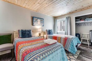 A bedroom with two beds, a wooden ceiling, a wall-mounted artwork, a window with curtains, and a closet with folded clothes. - Ski, Soak & Relax | Cozy Beech Mountain Condo (Beech Mountain)