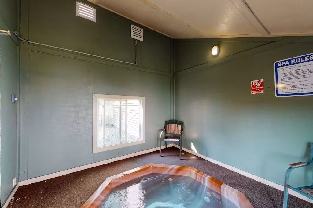 A spa room with a hot tub, a window, and a chair.