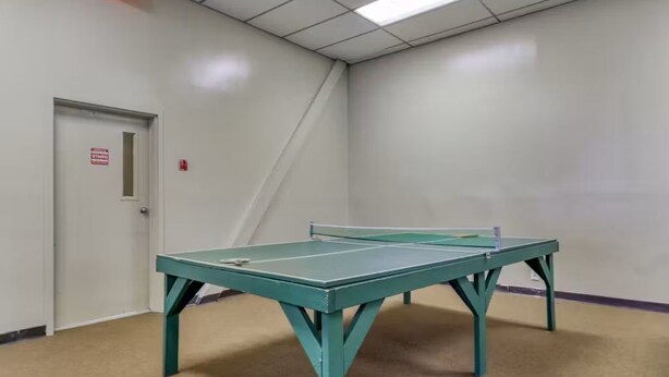 A room with a green ping pong table, a door with a 'No Smoking' sign, and a carpeted floor. - Ski, Soak & Relax | Cozy Beech Mountain Condo (Beech Mountain)