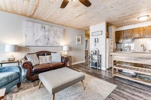 A cozy living room with a leather sofa, a matching ottoman, and a blue armchair. A wooden ceiling fan is visible, and the room features a large abstract painting on the wall. - Ski, Soak & Relax | Cozy Beech Mountain Condo (Beech Mountain)