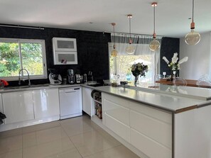 A modern kitchen with white cabinetry, a dishwasher, a coffee machine, and a large window with a view of greenery. - A house in the heart of the Camargue. Perfect for a vacation with family or friends (Aimargues)