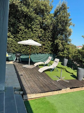 A deck with two lounge chairs and a barbecue grill, surrounded by trees and a green lawn. - A house in the heart of the Camargue. Perfect for a vacation with family or friends (Aimargues)
