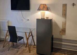 A room with a glass table, a chair, a standing lamp, a television mounted on the wall, and a radiator. - Elycon House Bergamo (Bergamo)