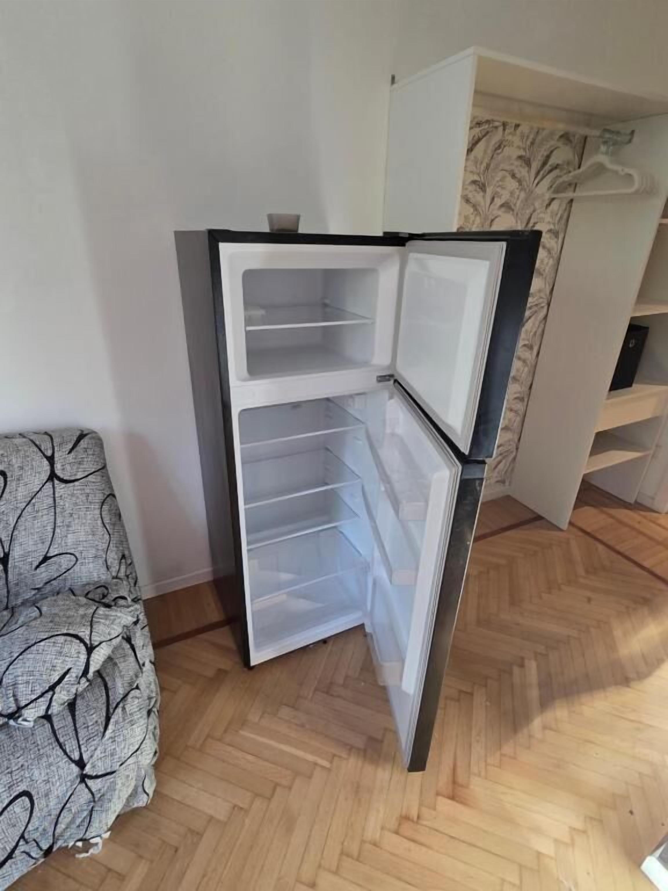 Un frigorifero compatto con vano congelatore, in una stanza con pavimento in legno a parquet e parete decorata.