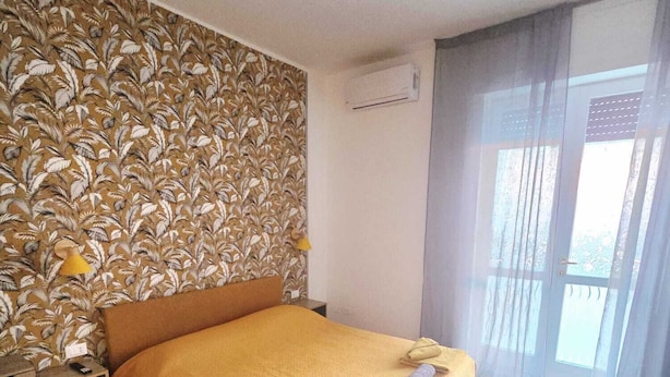 Un dormitorio con papel tapiz estampado, una cama con colcha amarilla, una lámpara de noche y una alfombra estampada.
