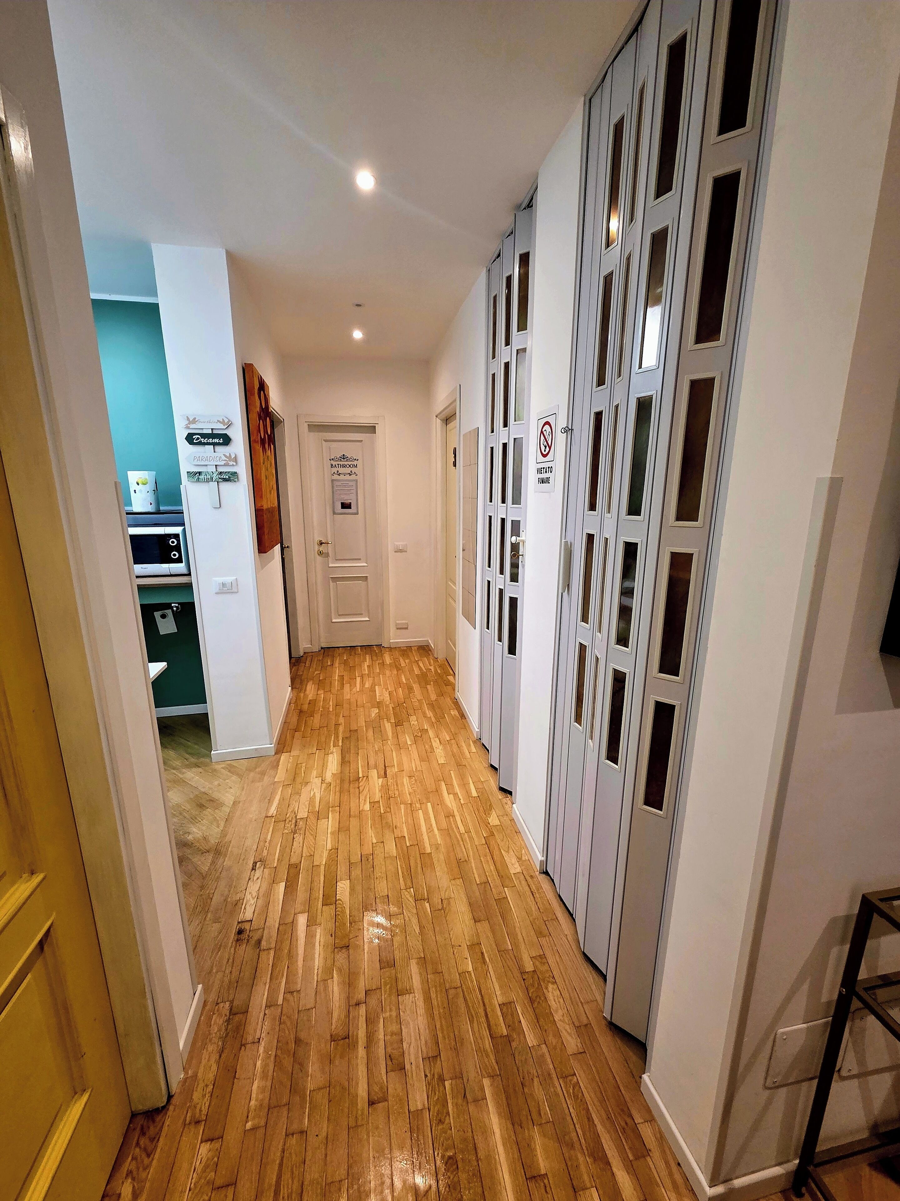 Un corridoio con pavimento in legno, pareti bianche e una porta con la scritta 'Bathroom'.