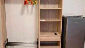 Una habitación compacta con un armario de madera, un tendedero de metal negro y un refrigerador negro.