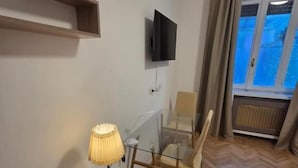 Habitación moderna con piso de madera, una mesa de vidrio, una silla, un televisor montado en la pared y una ventana con cortinas.
