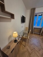 A modern room with a wooden floor, a glass table, a chair, a TV mounted on the wall, and a window with curtains.