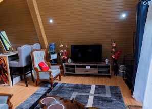 A living room with a large flat-screen TV, two armchairs, a coffee table, and a wooden ceiling. - Beautiful cabin in a substantial green space perfect for unwinding & recharging (Kisumu)