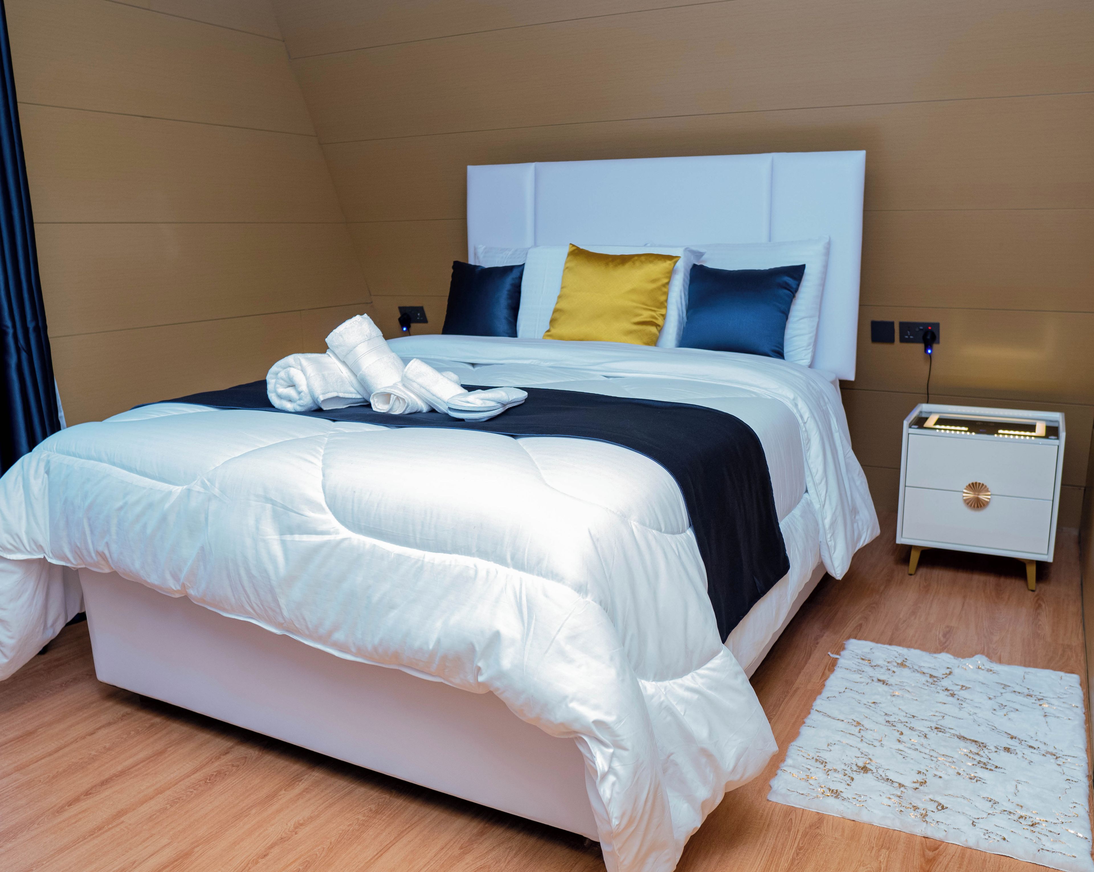 A hotel room with a bed, a nightstand, and a bedside table.