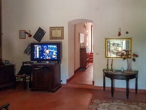 Un salon avec un téléviseur, un certificat encadré accroché au mur, un escalier menant à une autre pièce et une petite table sur laquelle est posé un vase.