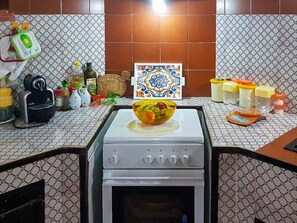 Une cuisine équipée d’une cuisinière, avec un saladier de fruits et divers ustensiles de cuisine disposés sur le plan de travail.
