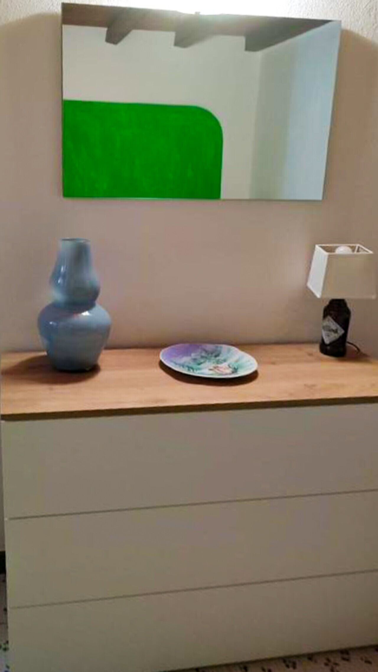 Une pièce comprenant une commode en bois, un vase, une assiette, une lampe et un miroir.