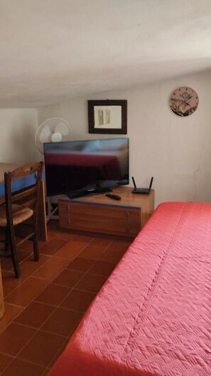 Ein Schlafzimmer mit einem Bett, einem Fernseher, einem Schreibtisch und einem Sessel.