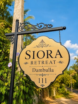 A wooden sign with the text 'SIORA RETREAT Dambulla 111' mounted on a metal post.