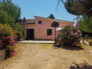 A single-story building with a flat roof, a front door, and a basketball hoop in the yard. - Gisella's House (Sicilia)