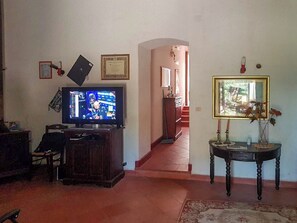 Ein Wohnzimmer mit Fernseher, einem gerahmten Zertifikat an der Wand und einem kleinen Tisch mit Kerze und Blumenvase.