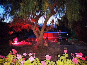 A tree with a structure behind it, possibly a gazebo or shed, surrounded by flowering plants. - Gisella's House (Sicilia)
