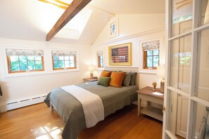 A bedroom with a bed, a nightstand, a lamp, a window with a curtain, and a framed picture on the wall.