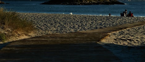 A wooden boardwalk leading to a sandy beach with a small island in the distance.