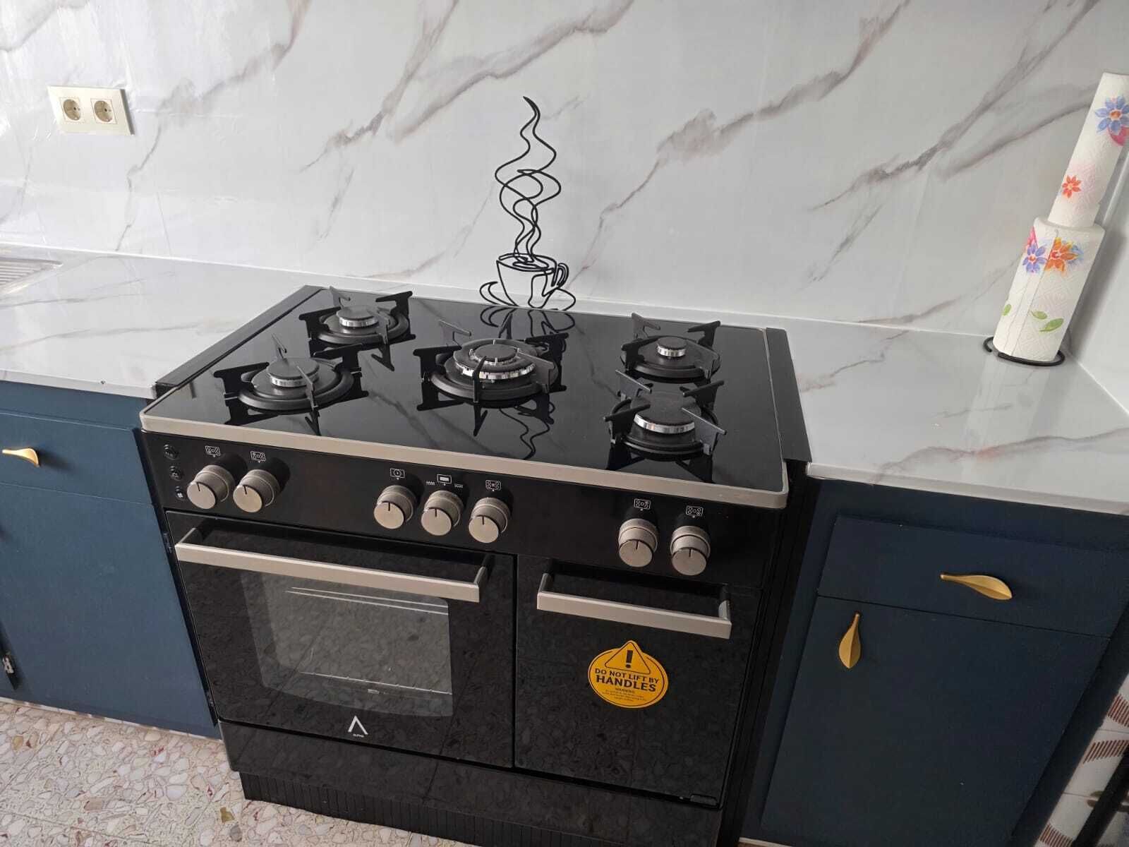 Estufa negra con cuatro hornillas y horno integrado, ubicada en una cocina con encimeras de mármol y muebles oscuros.