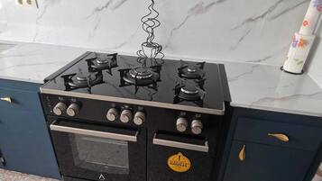 Estufa negra con cuatro hornillas y horno integrado, ubicada en una cocina con encimeras de mármol y muebles oscuros.