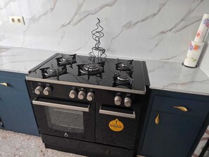 A black stove with four burners and a built-in oven, located in a kitchen with marble countertops and dark cabinetry.