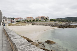 A coastal hotel with multiple floors, a sandy beach, and a rocky shoreline.