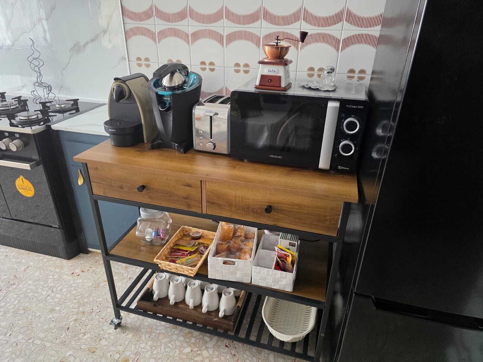 Una kitchenette equipada con estufa a gas, cafetera, tostadora, microondas y un estante pequeño con utensilios de cocina y snacks.