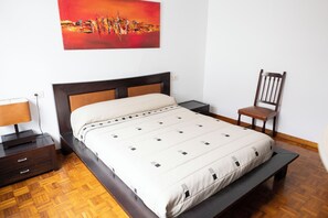 A neatly arranged bedroom with a bed, bedside table, chair, and a painting on the wall.
